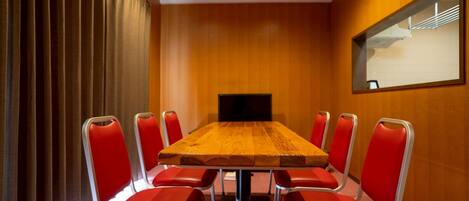 A conference room with a wooden table, red chairs, a television, and a mirror on the wall.