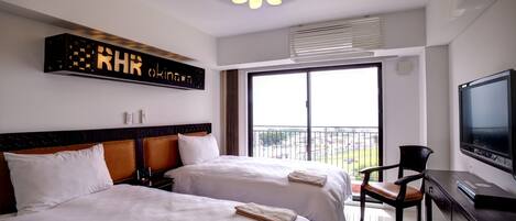 A hotel room with two beds, a TV, a desk, and a balcony with a view.