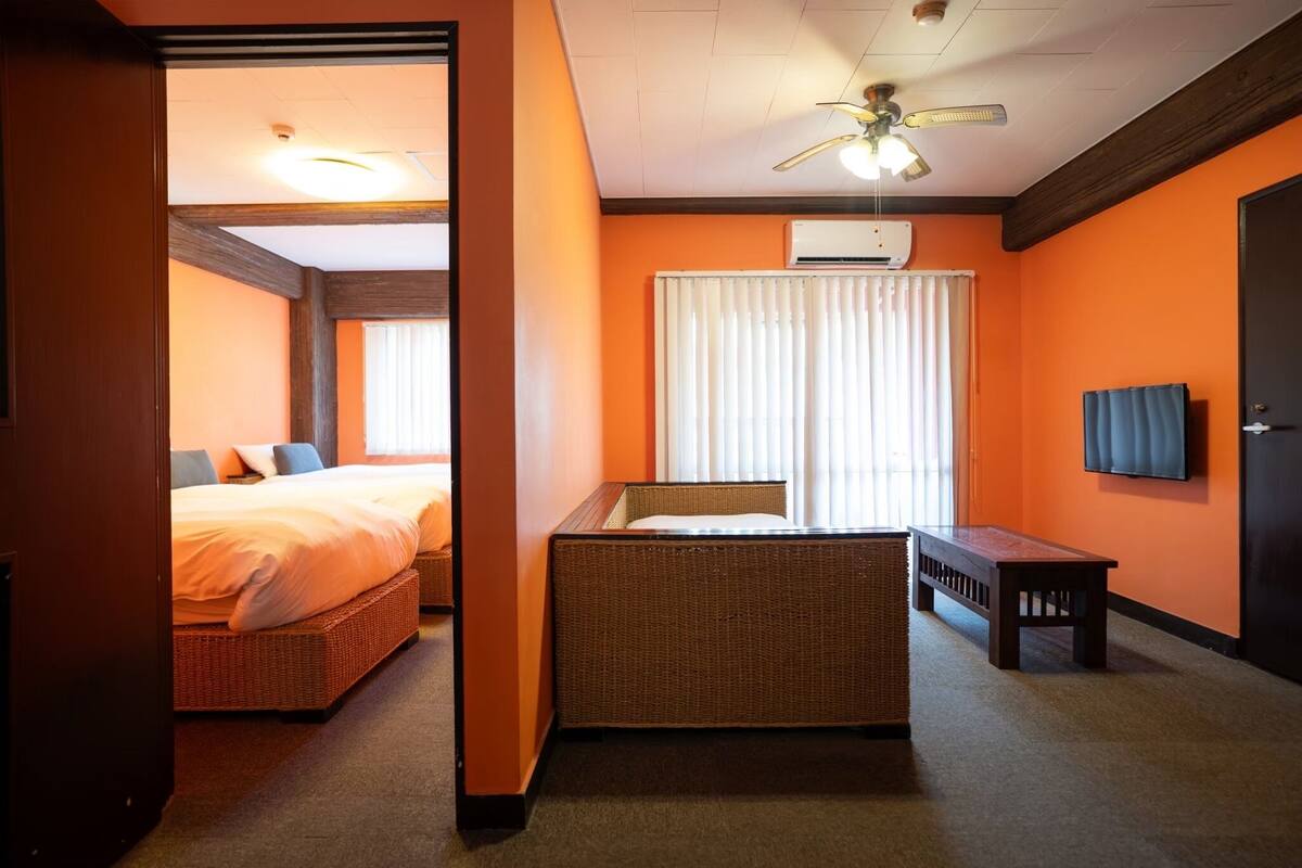 A hotel room with a bed, a small seating area, a window with curtains, and a ceiling fan.