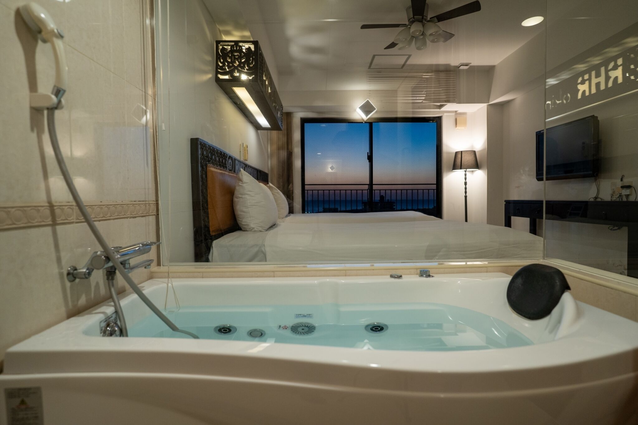 Ein Hotelzimmer mit einer großen Badewanne, einem Bett mit Blick auf den Sonnenuntergang, einem Deckenventilator und einem Fernseher.