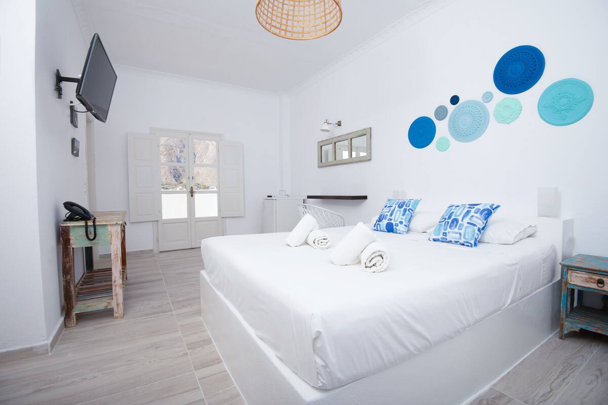 Une chambre avec un lit, un téléviseur fixé au mur, une petite table avec un téléphone et une fenêtre donnant sur un beau paysage.