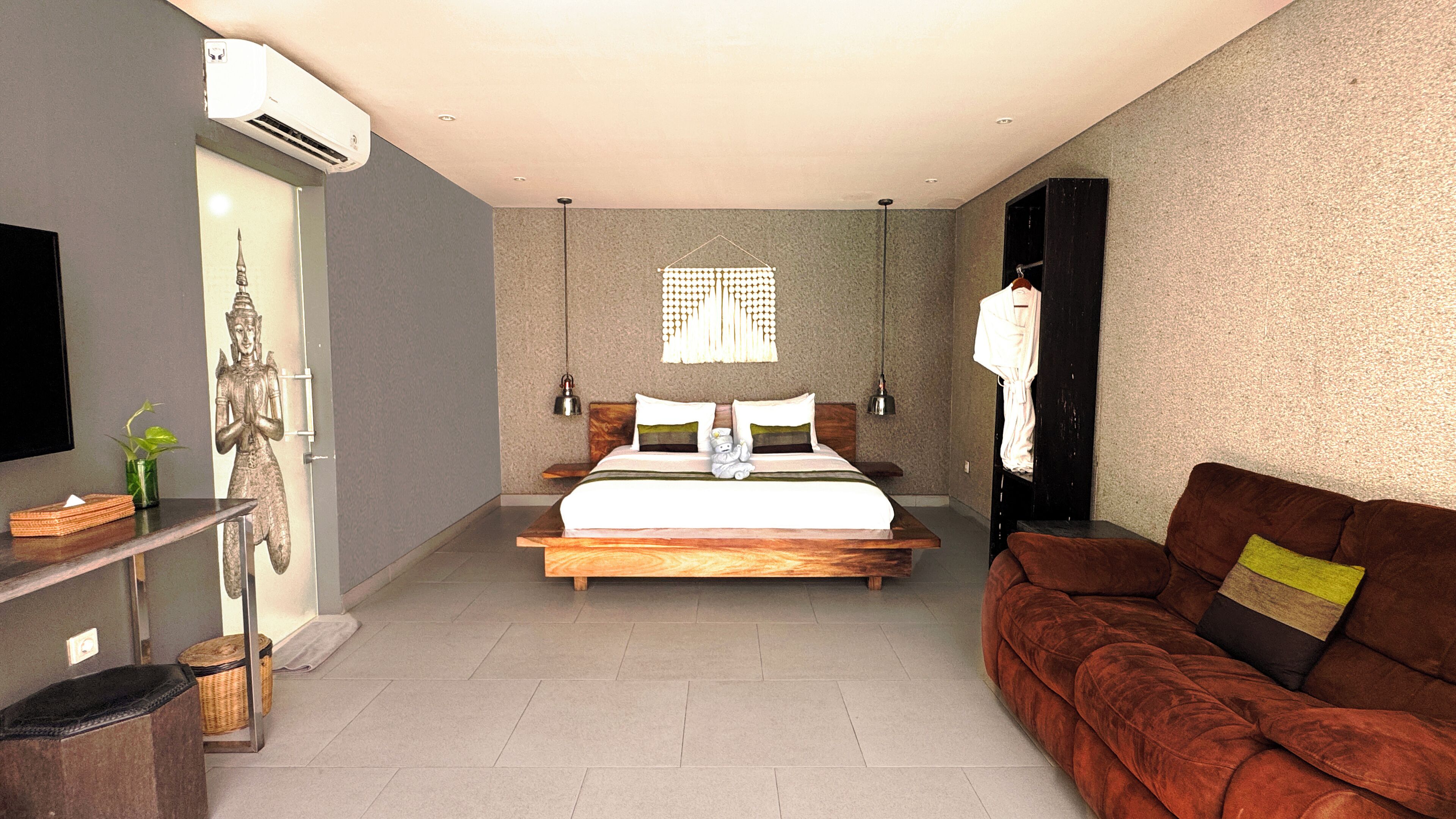 Un dormitorio con una cama grande, una mesita de noche de madera, un sofá marrón, un televisor y un aire acondicionado instalado en la pared.