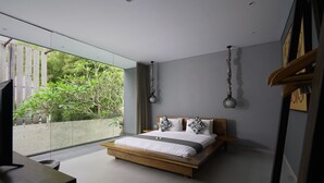 A modern bedroom with a large bed, a wooden headboard, and a view of greenery outside. - Sandhya Villa (Canggu)