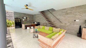A modern living room with a wooden sofa, a dining area, and a spiral staircase against a textured wall. - Sandhya Villa (Canggu)
