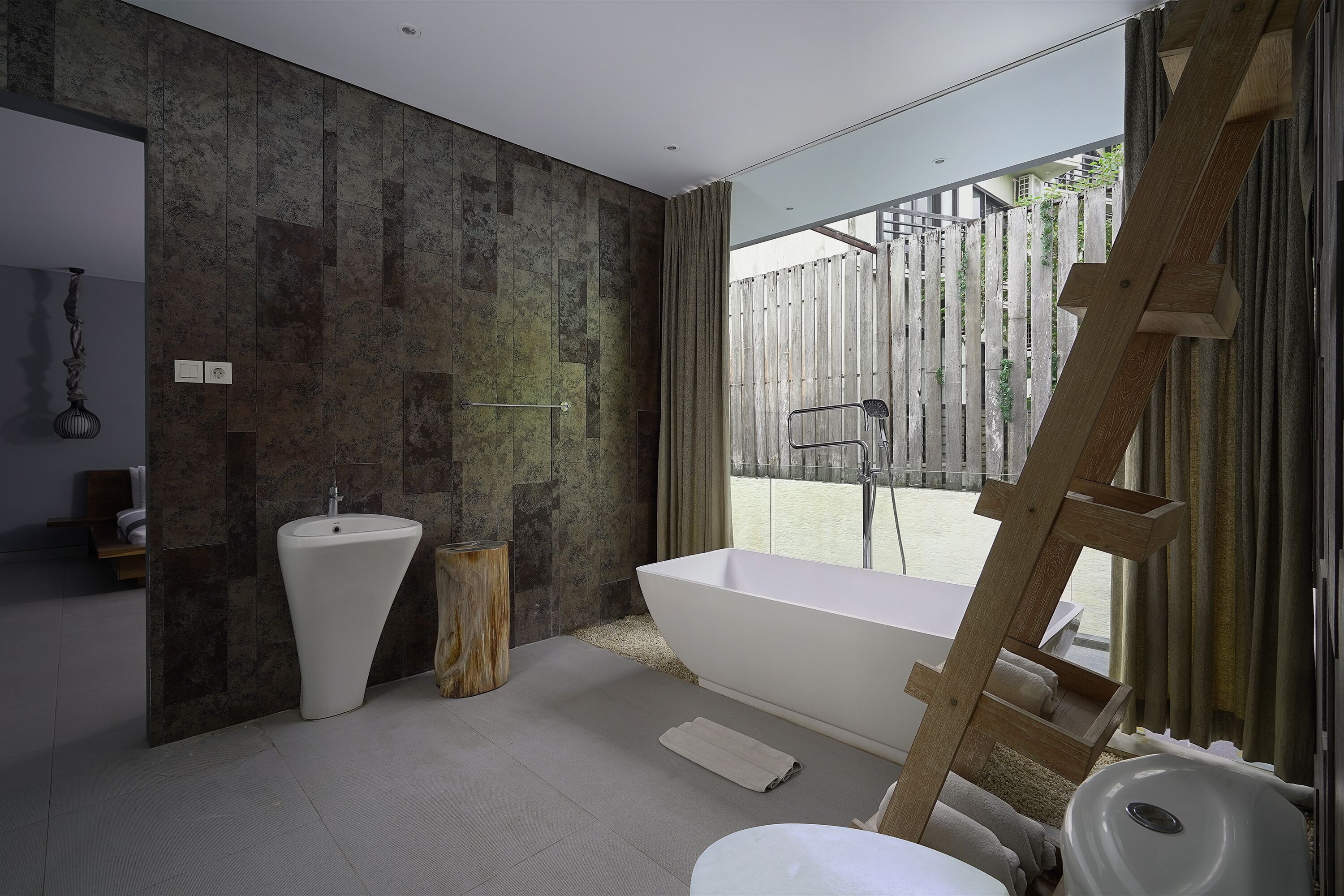 A modern bathroom with a freestanding bathtub, a sink, and a wooden stool.