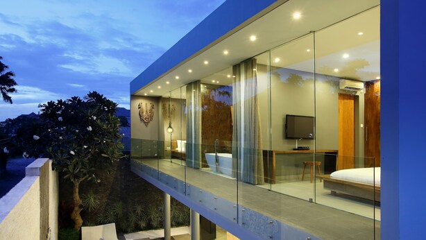 A modern hotel room with a glass balcony, a bathtub, a TV, and a wooden wardrobe. - Sandhya Villa (Canggu)