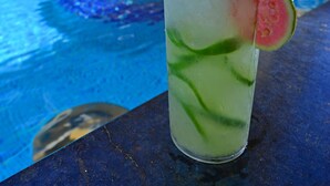 A glass of a tropical drink with a slice of fruit, placed on a table by a poolside with a building in the background. - Pousada Doce Cabana (Ipojuca)