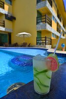 Un vaso de una bebida tropical con una rodaja de fruta, sobre una mesa junto a una piscina, con un edificio al fondo.