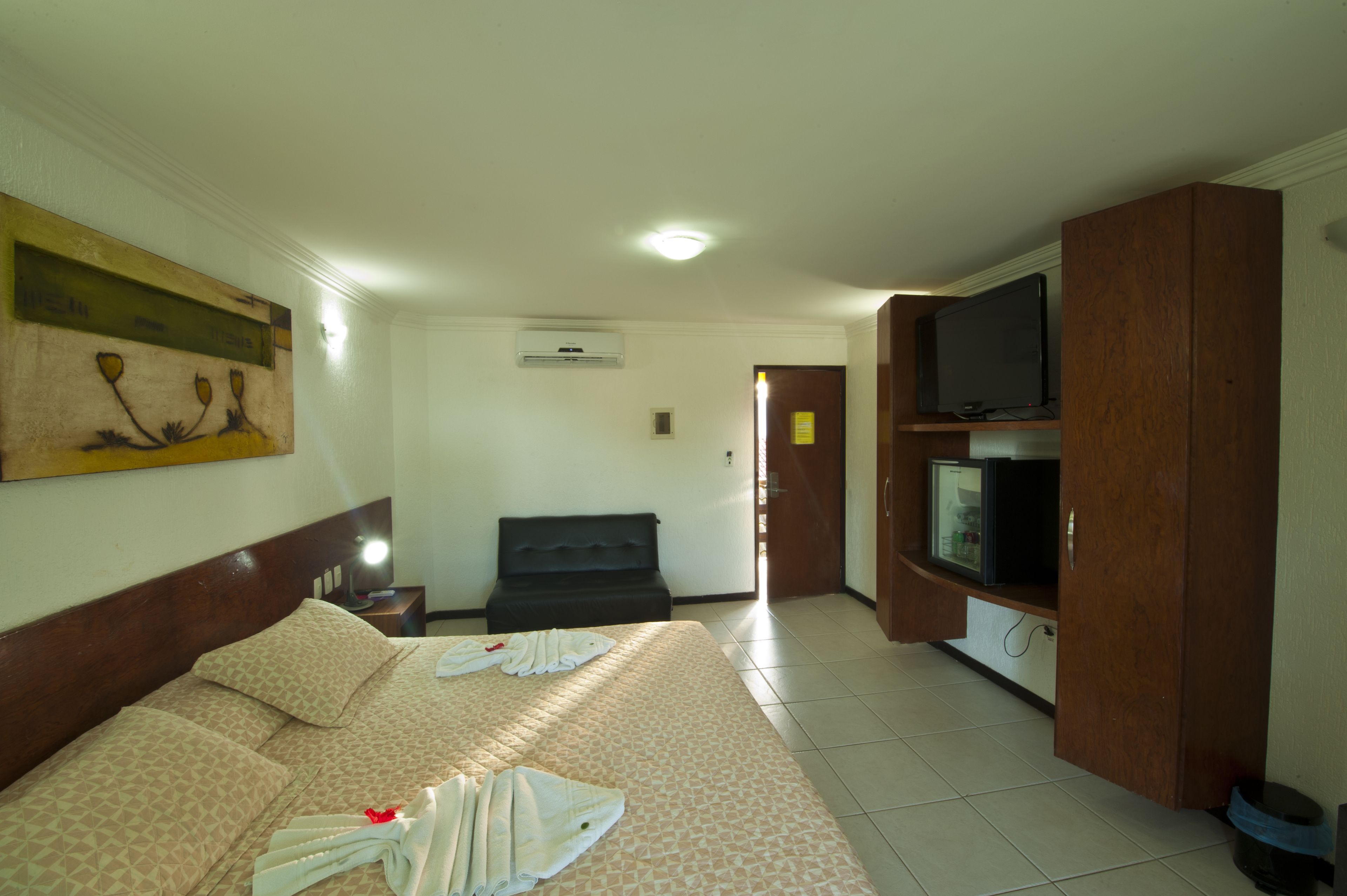 A hotel room with a bed, a television, a desk, and a wall-mounted artwork.