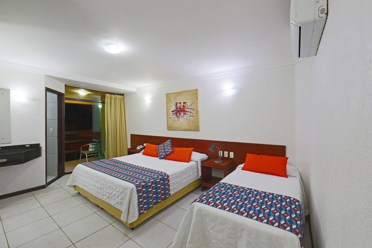 Quarto de hotel com duas camas, uma escrivaninha, uma cadeira e um banheiro visível por uma porta aberta.