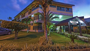 A hotel with a modern design, featuring a large glass facade, a covered entrance, and a well-maintained lawn with palm trees. - Pousada Doce Cabana (Ipojuca)