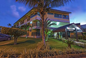Hotel de diseño moderno, con fachada de vidrio amplia, entrada cubierta y césped bien cuidado con palmeras.