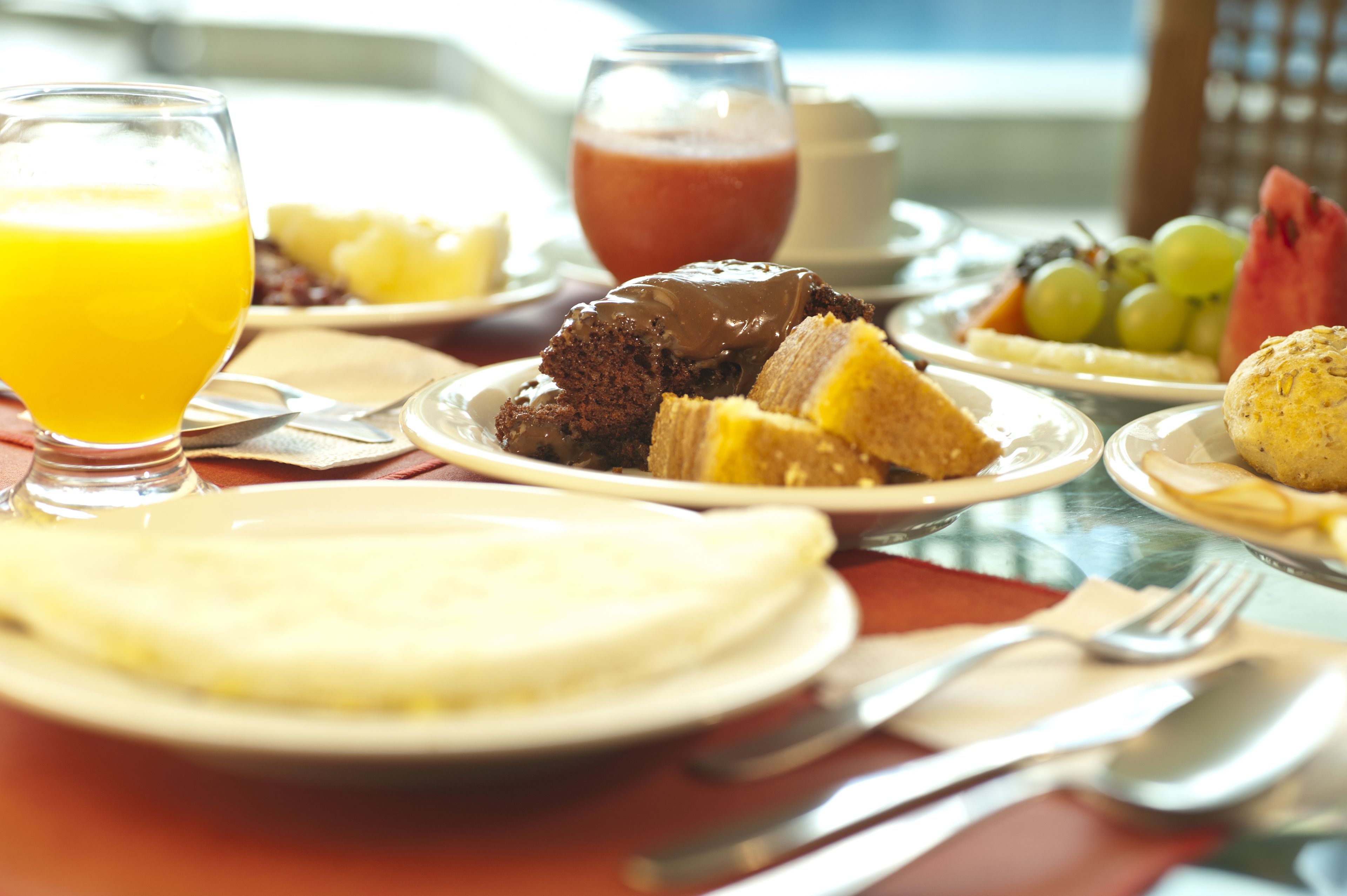 Ein Frühstückstisch mit verschiedenen Speisen, darunter Pfannkuchen, ein Glas Orangensaft und ein Obstteller.