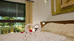 A hotel room with a bed, a window with a view of palm trees and a beach, and a wall with a framed picture. - Pousada Doce Cabana (Ipojuca)