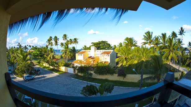 A view from a balcony overlooking a street lined with palm trees and a building with a tiled roof. - Pousada Doce Cabana (Ipojuca)