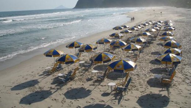 A beach with rows of beach umbrellas and lounge chairs. - Hotel Camburi Praia (São Sebastião)