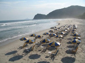A beach with rows of beach umbrellas and lounge chairs. - Hotel Camburi Praia (São Sebastião)