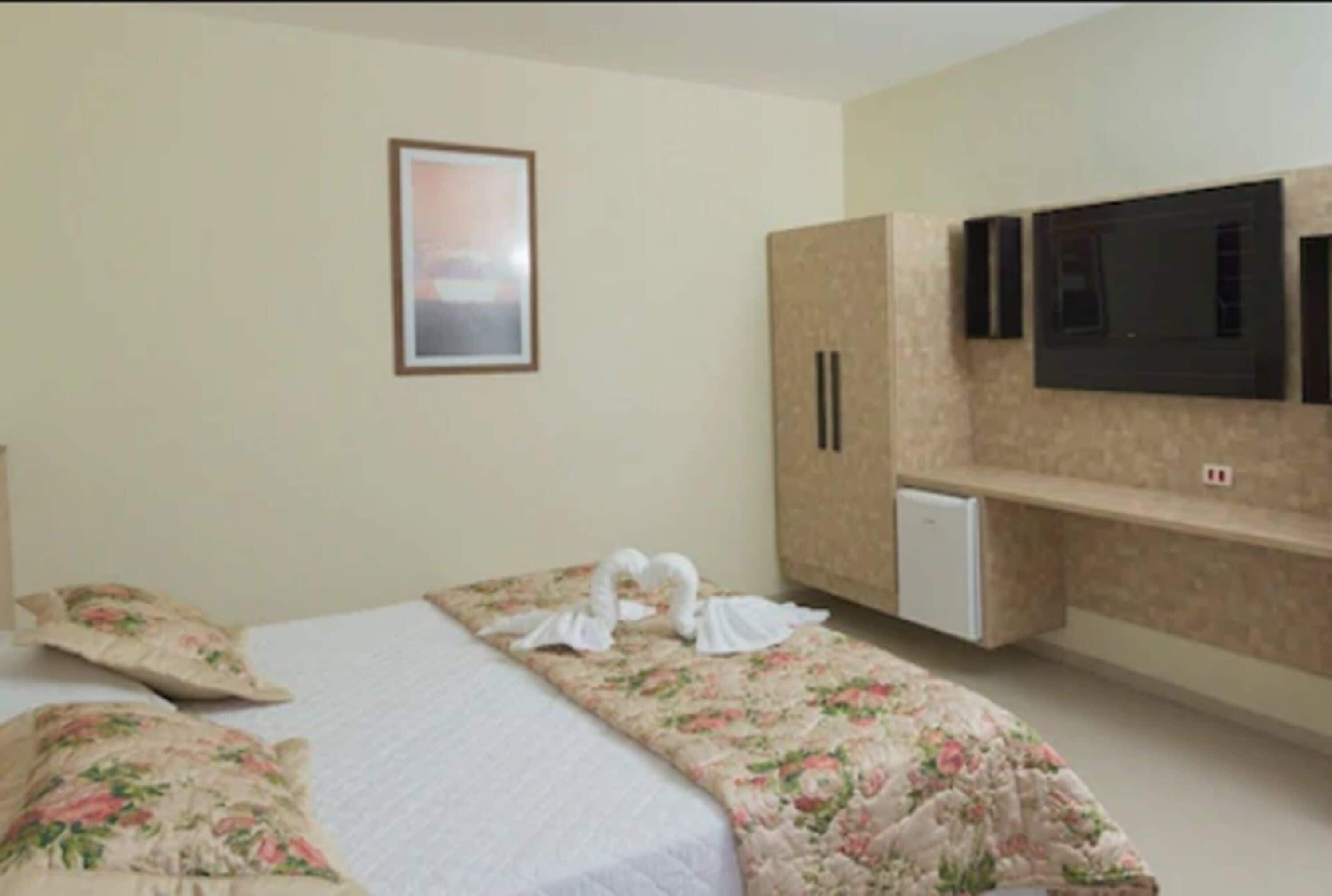 Habitación de hotel con dos camas, un televisor montado en la pared y una pequeña kitchenette.