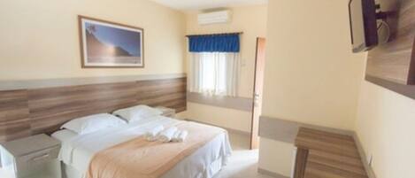 A hotel room with a bed, a nightstand, a ceiling fan, a mounted TV, and a window with curtains.
