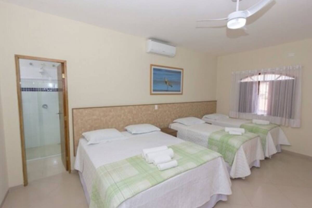 A hotel room with two beds, a shower, a ceiling fan, and a window with curtains.