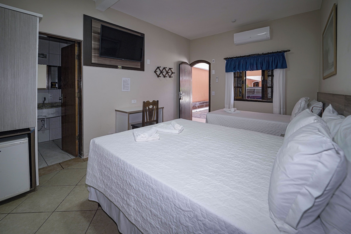 A hotel room with two beds, a desk, a chair, a TV, and a balcony.