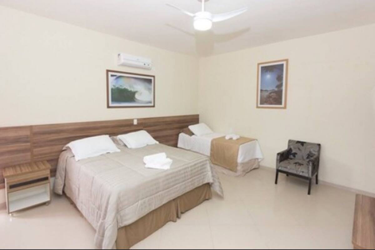 A hotel room with a large bed, a smaller bed, a chair, a nightstand, and a ceiling fan.