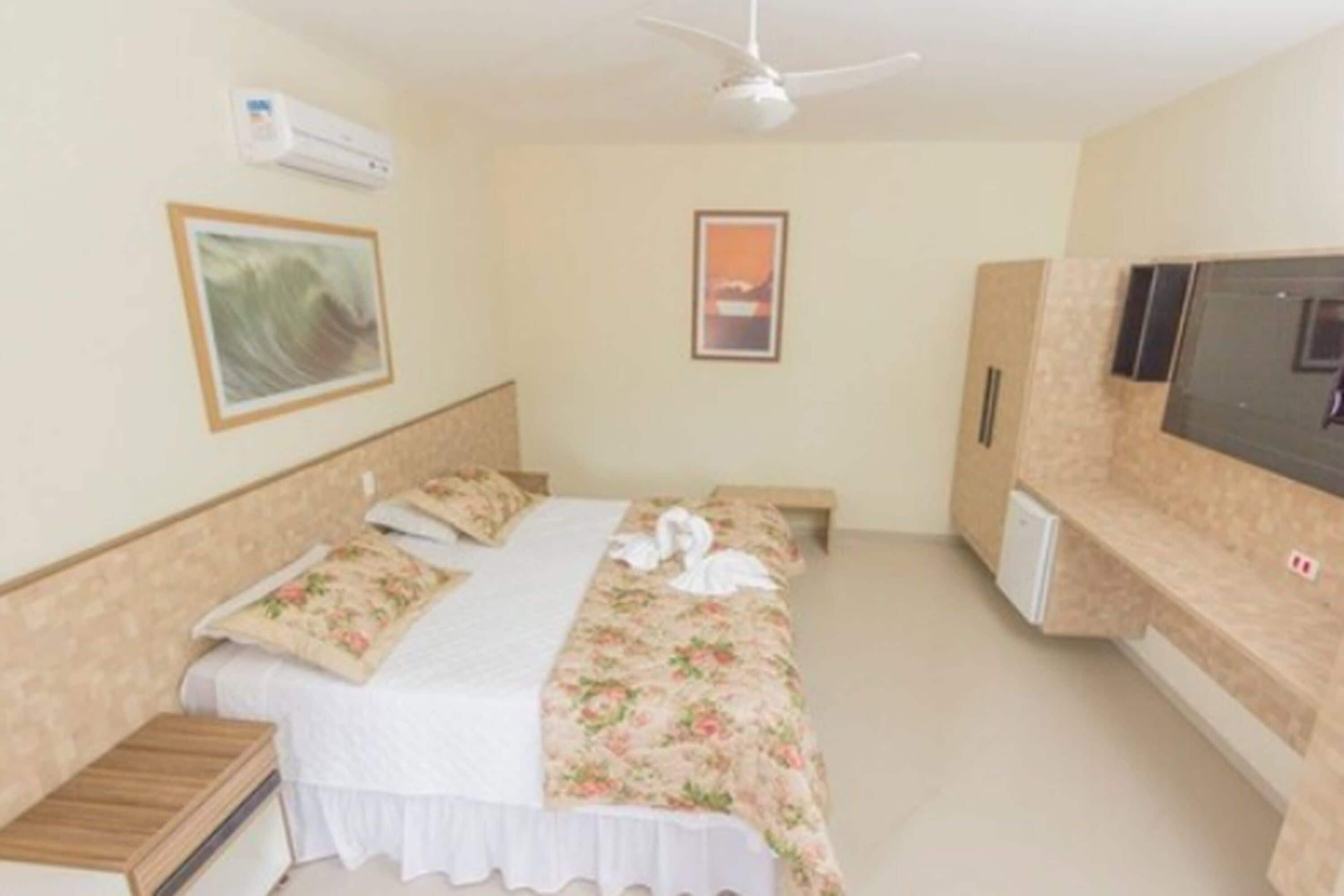 A bedroom with a bed, a bedside table, a TV, and a ceiling fan.