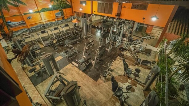 A gym with various exercise equipment, a mural on the wall, and wooden flooring. - Hotel Camburi Praia (São Sebastião)