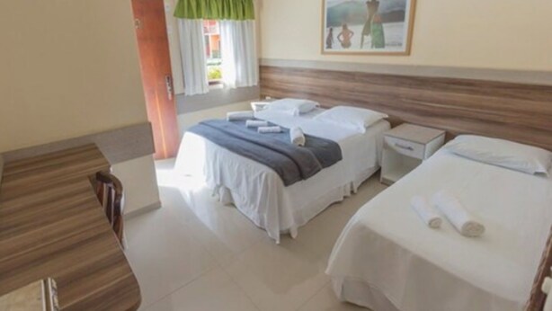 A hotel room with two beds, a wooden headboard, a window with curtains, a painting on the wall, and a small bedside table. - Hotel Camburi Praia (São Sebastião)