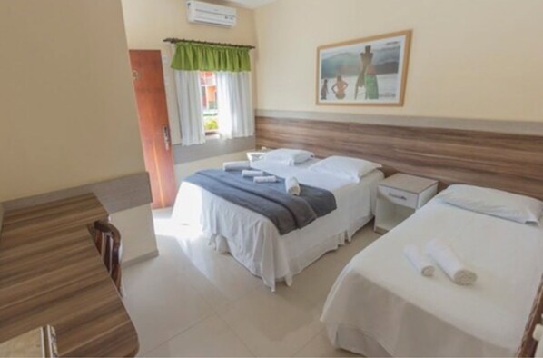 A hotel room with two beds, a wooden headboard, a window with curtains, a painting on the wall, and a small bedside table. - Hotel Camburi Praia (São Sebastião)