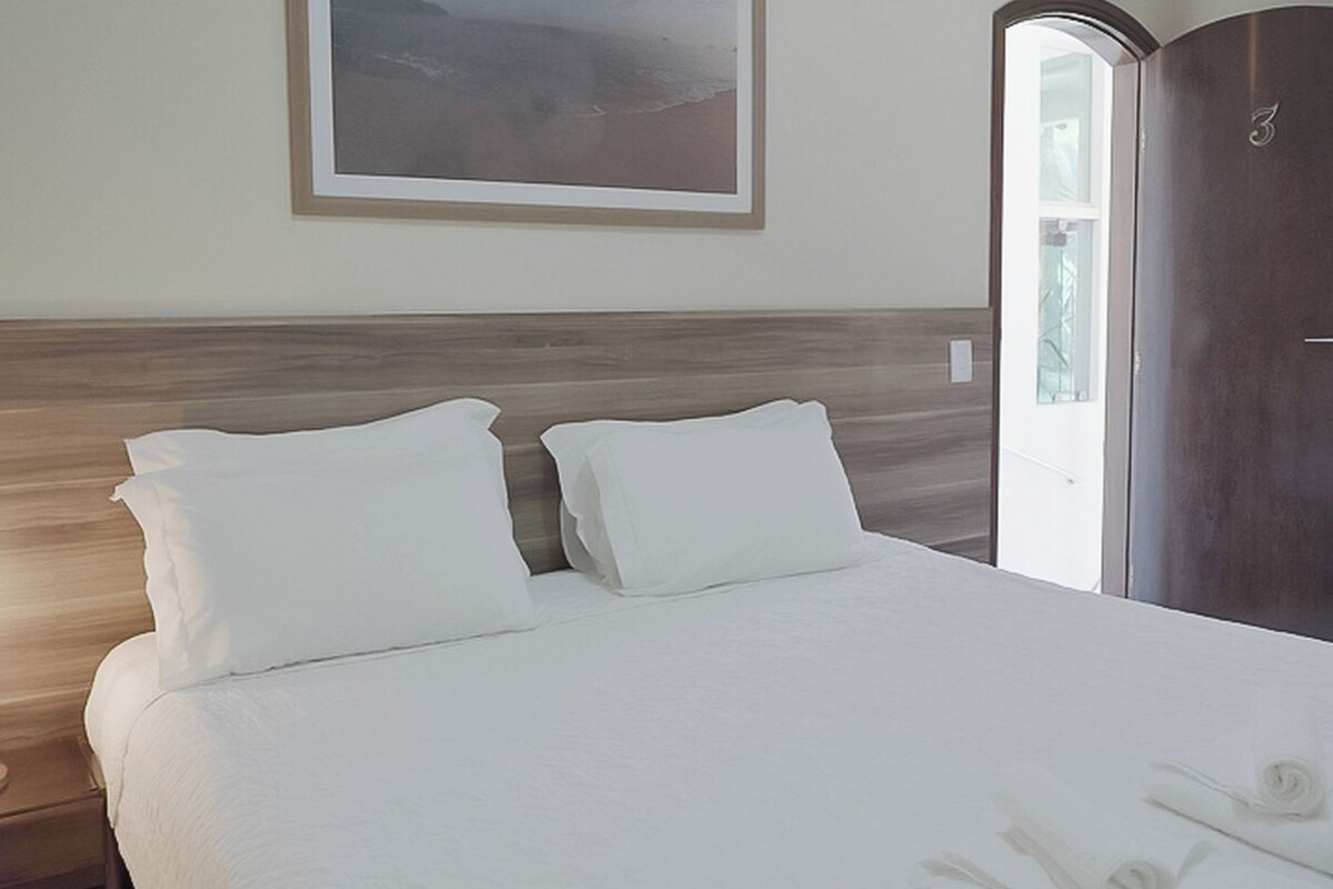 A neatly made bed with white linens, a wooden headboard, and a framed landscape painting on the wall.