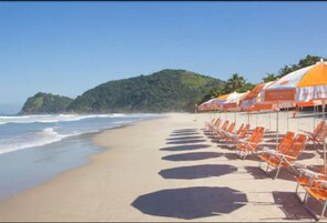 A beach with rows of orange beach chairs and umbrellas, a sandy shore, and a hilly landscape in the background.