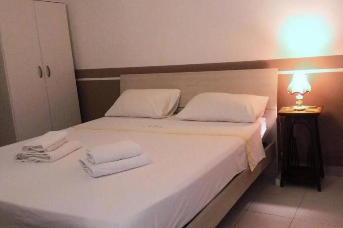 Un lit bien fait, avec du linge de lit blanc et des oreillers, une lampe de chevet et une armoire dans une chambre d’hôtel.