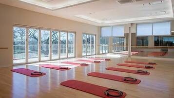A spacious room with large windows, wooden floors, and red exercise mats arranged for group activities.