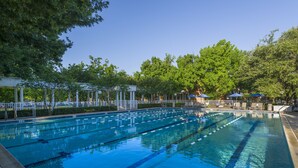 A swimming pool with clear lanes, surrounded by trees and shaded areas with umbrellas. - Cooper Hotel Conference Center & Spa (Dallas)