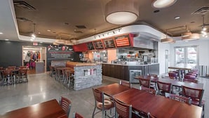 A modern restaurant interior with wooden tables and chairs, a kitchen area, and a counter with menu boards. - Cooper Hotel Conference Center & Spa (Dallas)