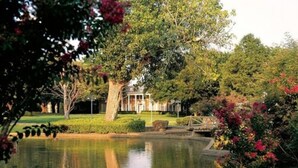 A serene pond with a bridge, surrounded by lush greenery and flowering plants. - Cooper Hotel Conference Center & Spa (Dallas)