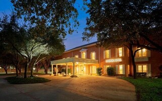 Een hotel met een overdekte ingang, een bord waarop "COOPER HOTEL" staat en een goed verlichte gevel.
