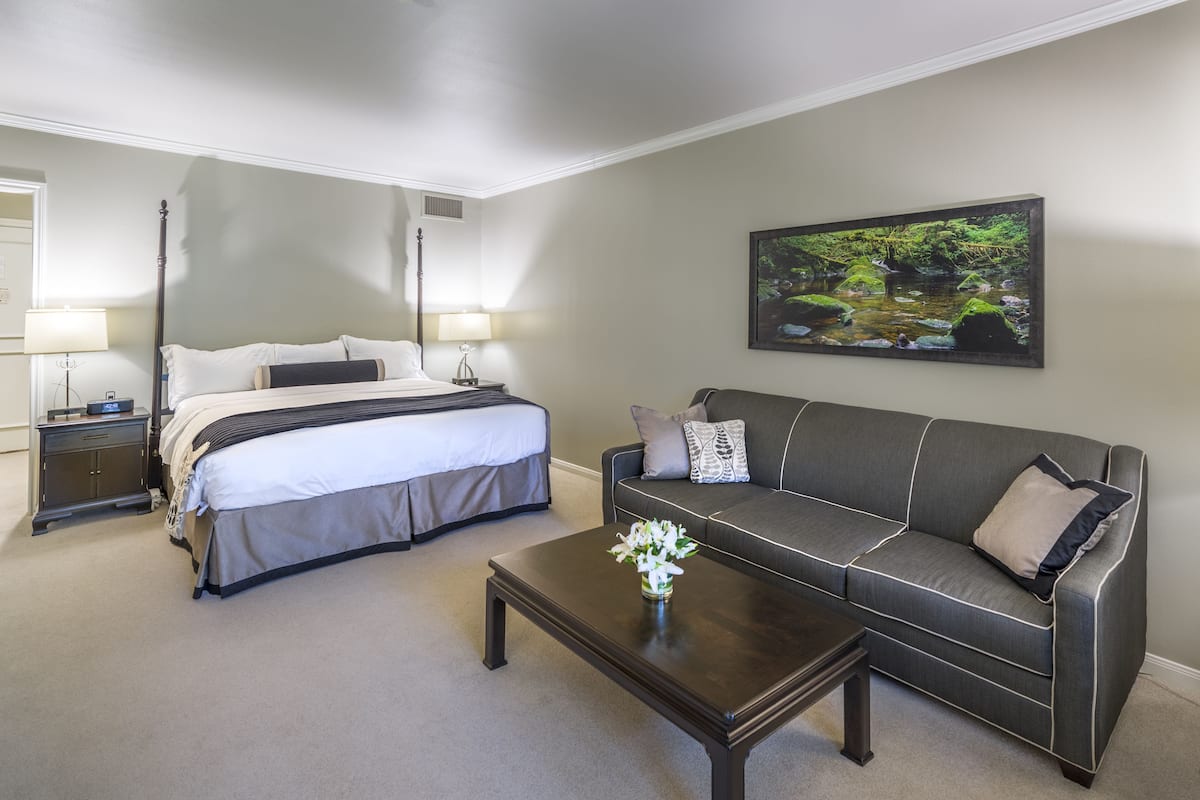 A hotel room with a bed, a sofa, a coffee table, and a painting on the wall.