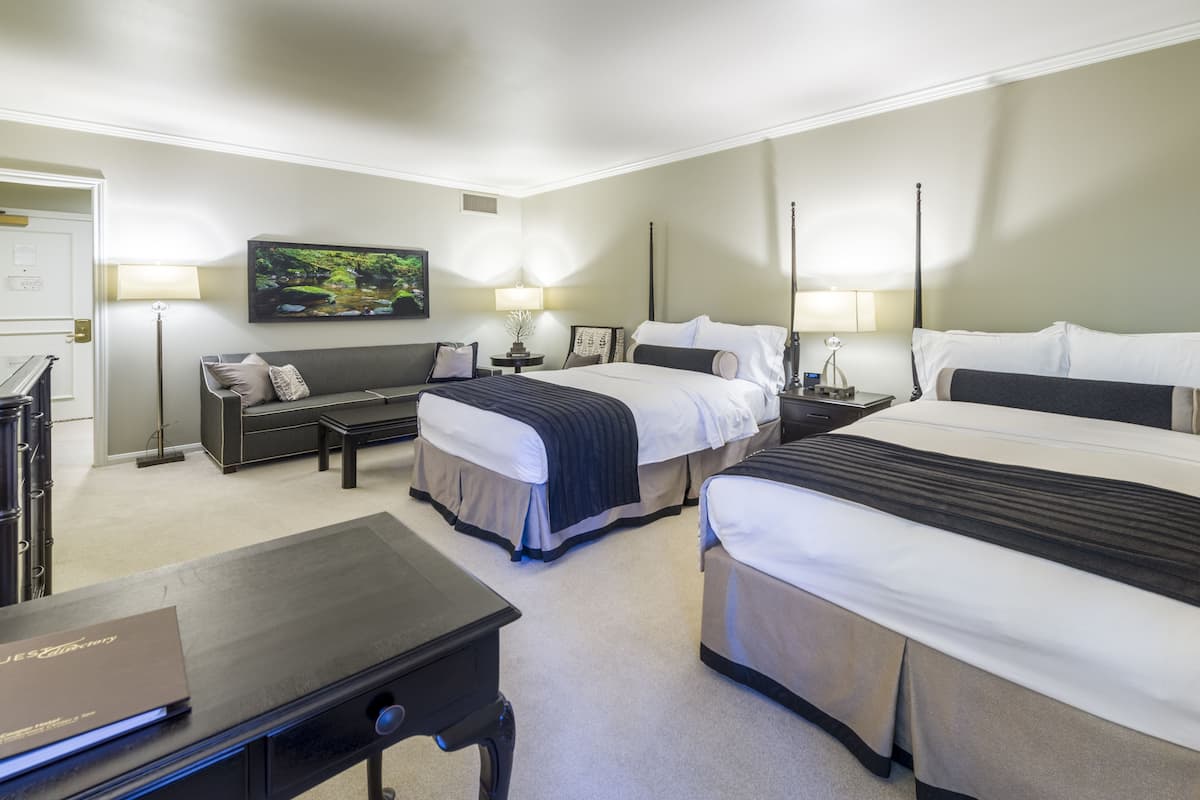A hotel room with two beds, a desk, a chair, and a painting on the wall.