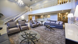 A spacious hotel lobby with a grand staircase, comfortable seating, and a chandelier. - Cooper Hotel Conference Center & Spa (Dallas)