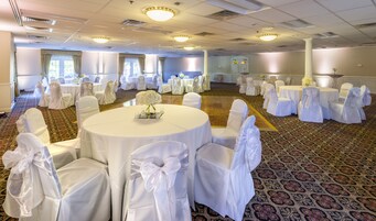 Un salón de banquetes con mesas redondas y sillas, manteles blancos y centros de mesa florales.