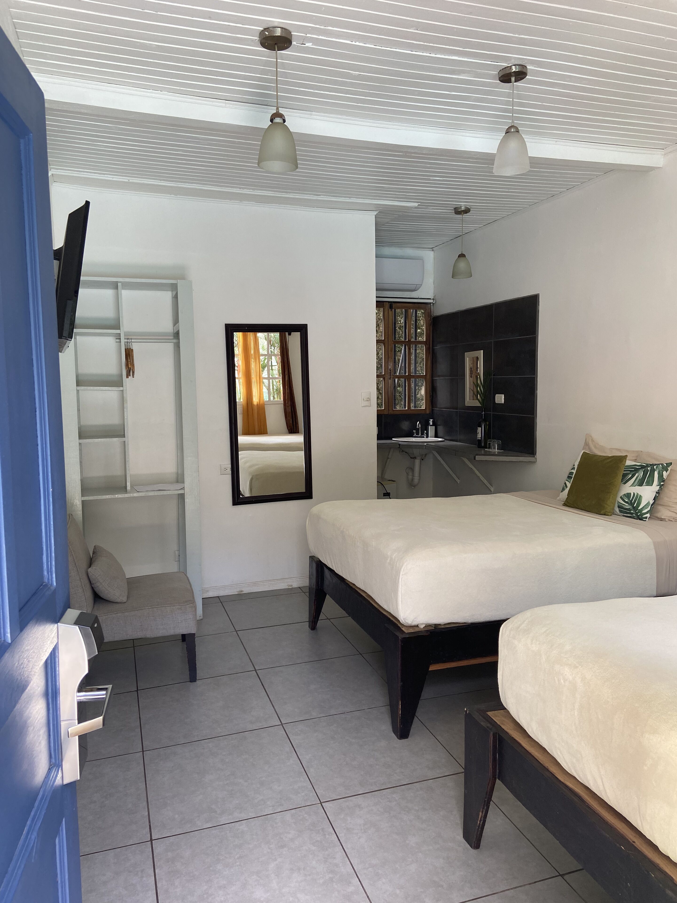Un dormitorio con dos camas, un armario, un espejo, un lavamanos y un ventilador de techo.