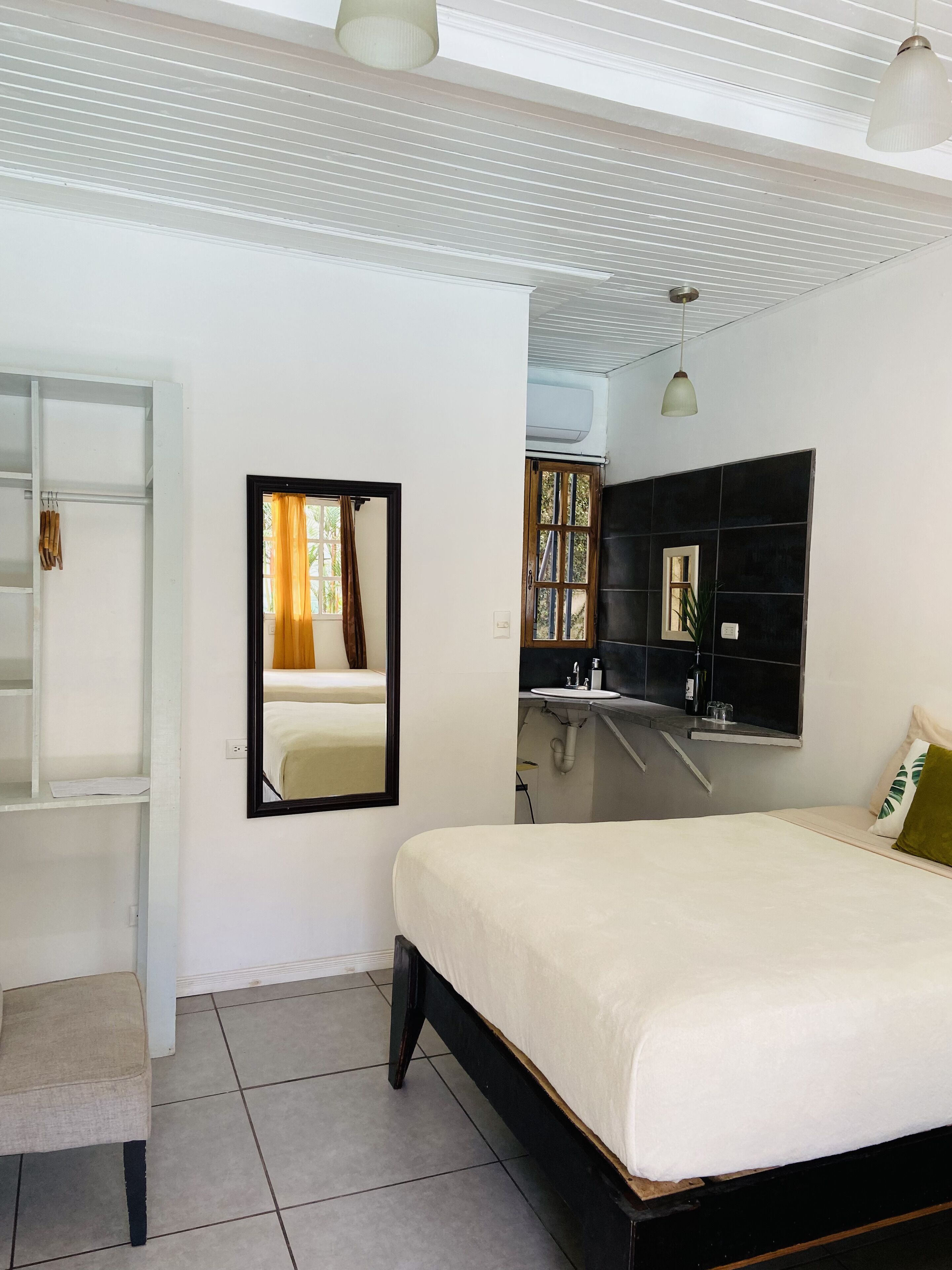 A bedroom with a bed, a wardrobe, a mirror, a sink, and a window with curtains.