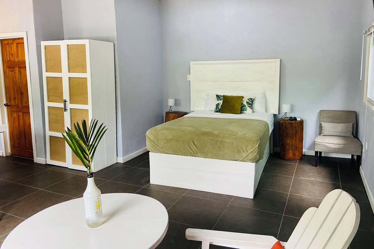 A bedroom with a bed, bedside tables, a chair, a table with a plant, and a wardrobe.