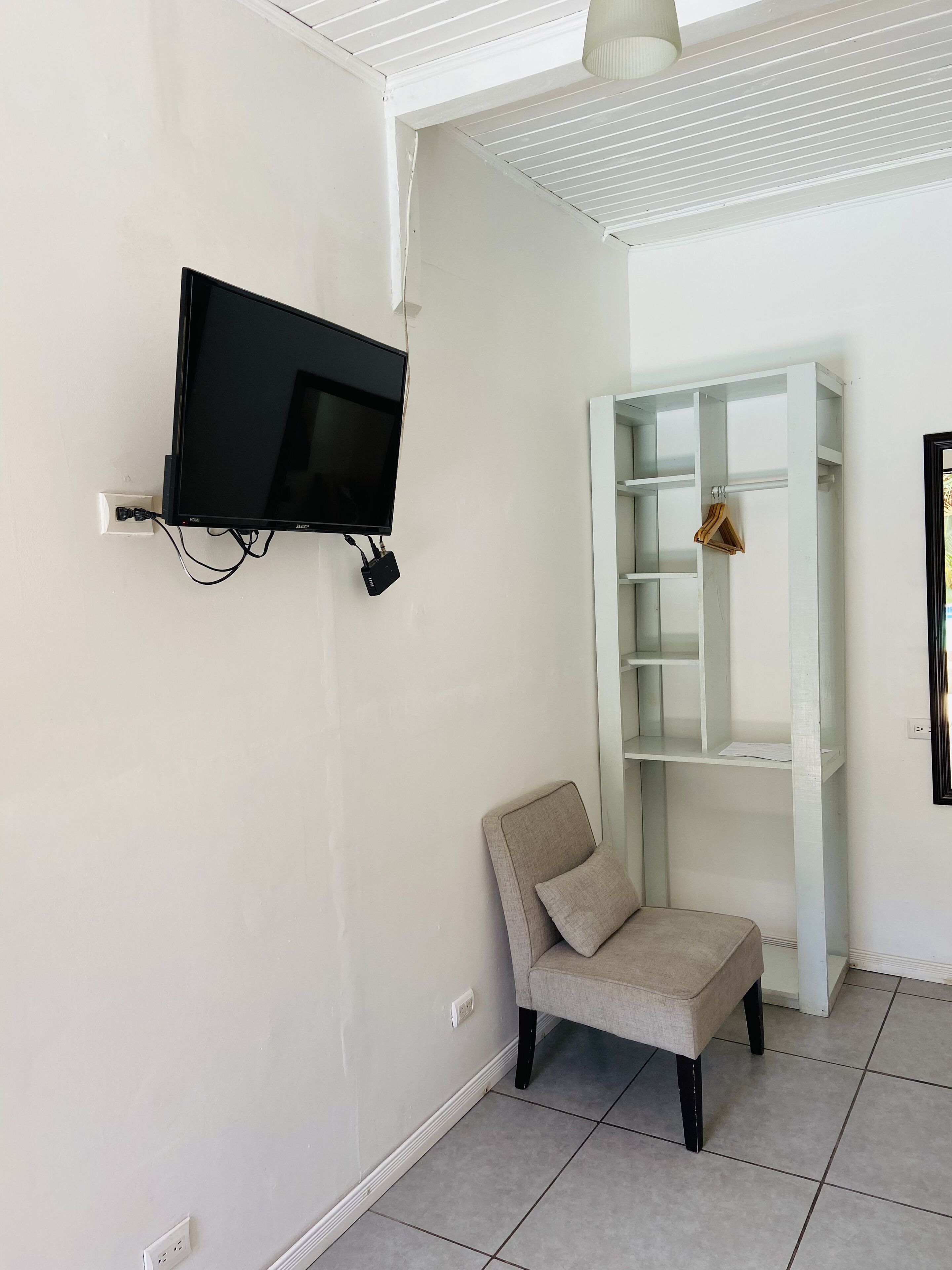Una habitación con televisor de pared, una silla y un estante blanco.