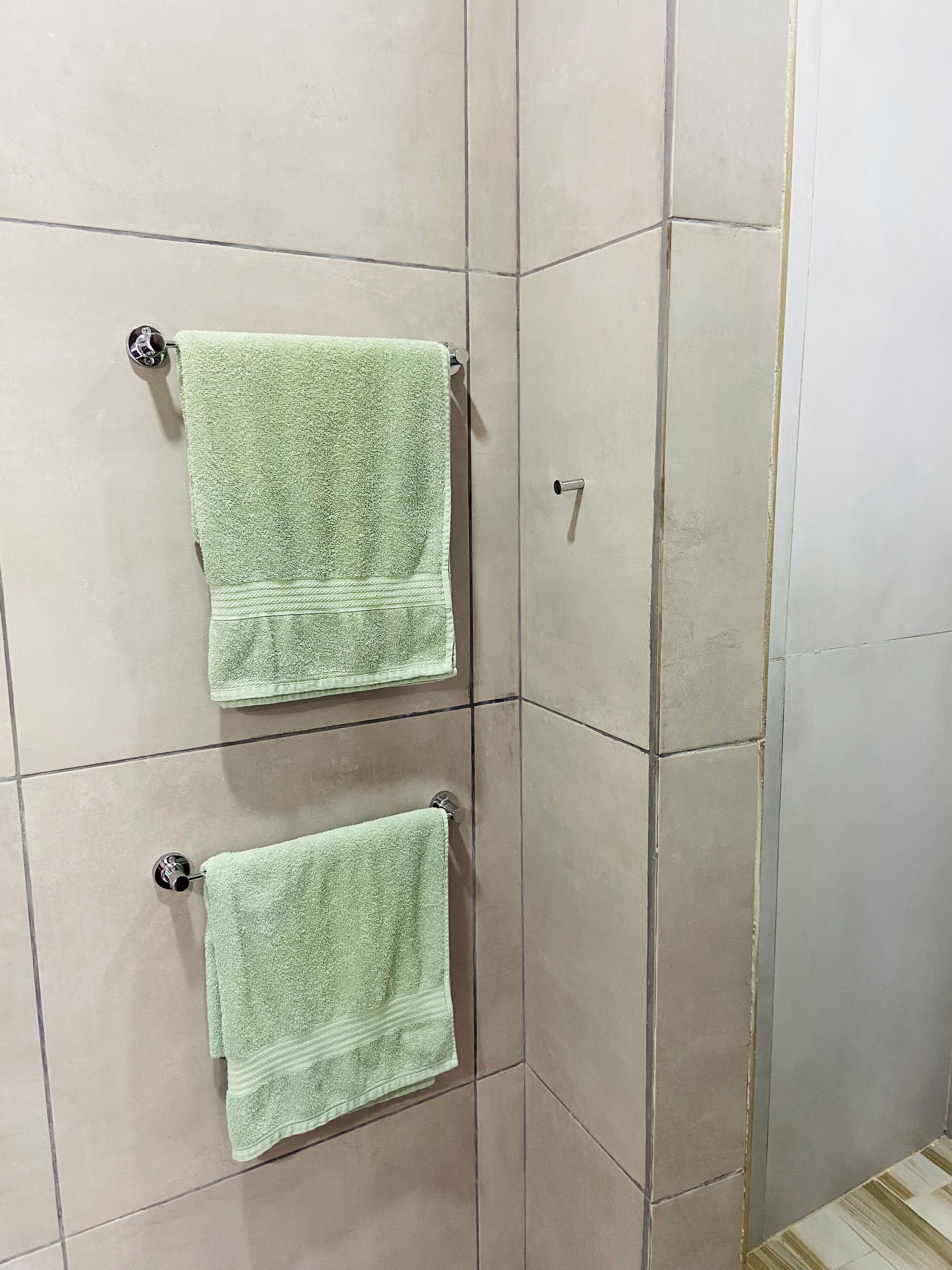 Un baño con dos toallas verdes colgadas en toalleros, paredes con azulejos color beige y una puerta con pomo plateado.