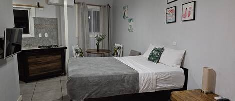 Une chambre à coucher avec un lit, une table de chevet et une petite table ronde agrémentée d’une plante.