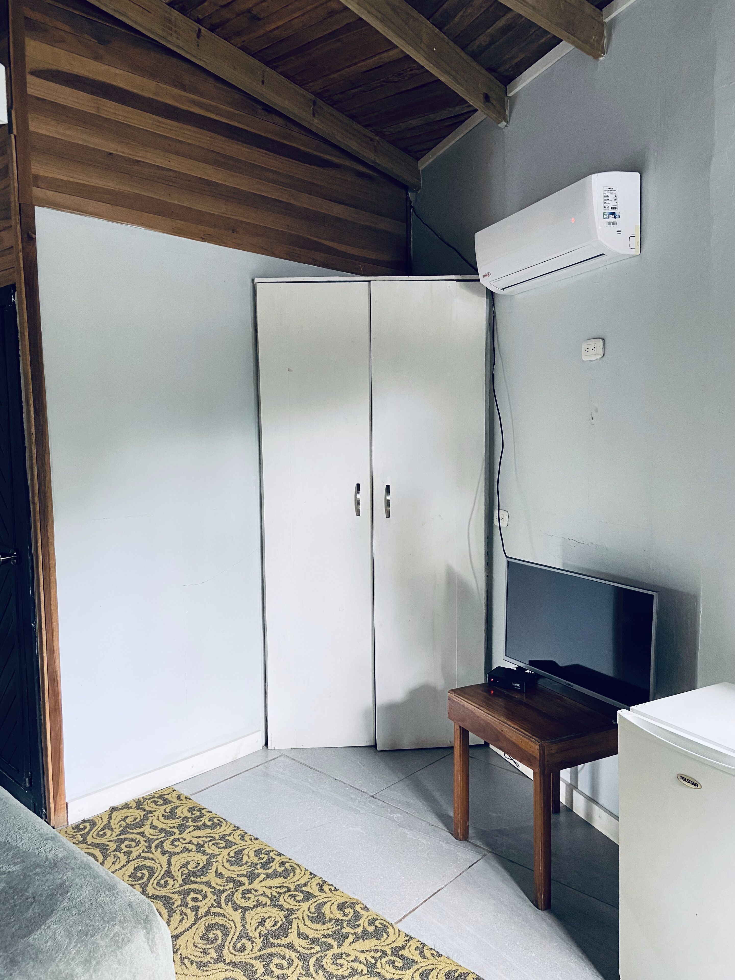 A room with a wardrobe, a television on a stand, and a small refrigerator.