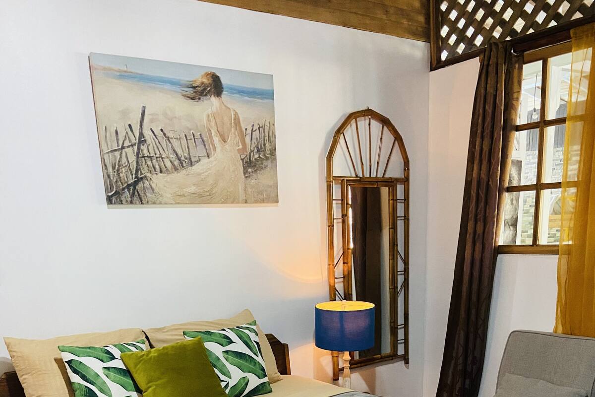 A bedroom with a bed, pillows, a nightstand, a lamp, a mirror, and a window with curtains.